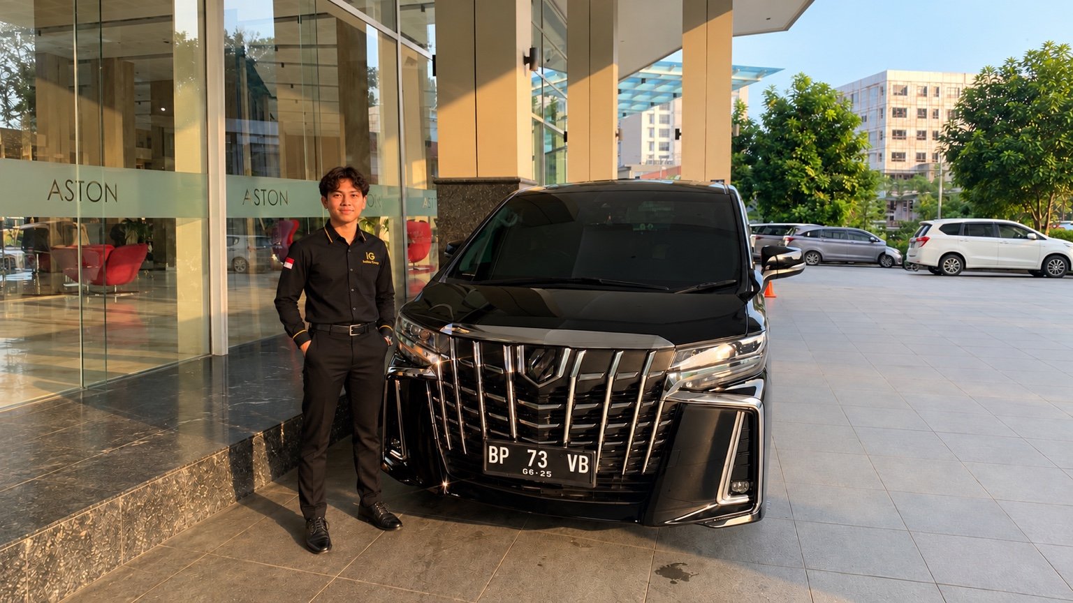 Pengemudi INDATU GROUP di samping Toyota Alphard hitam di Aston Batam.
